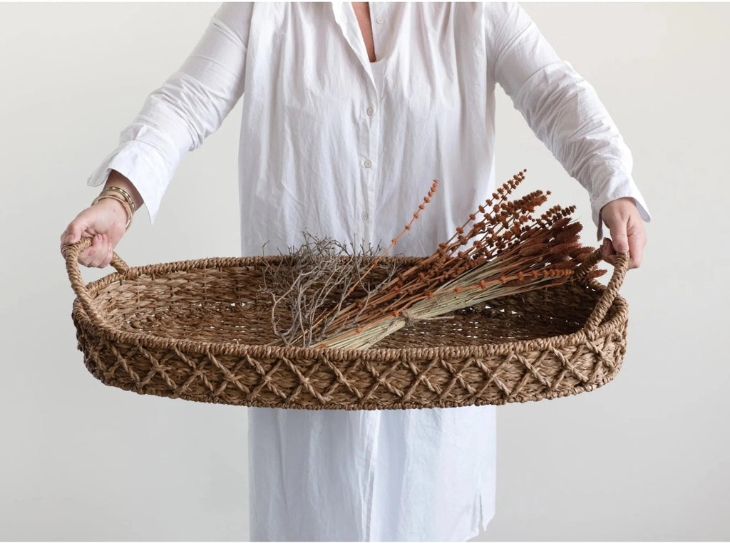 Person holding a woven tray with dried plants against a plain background